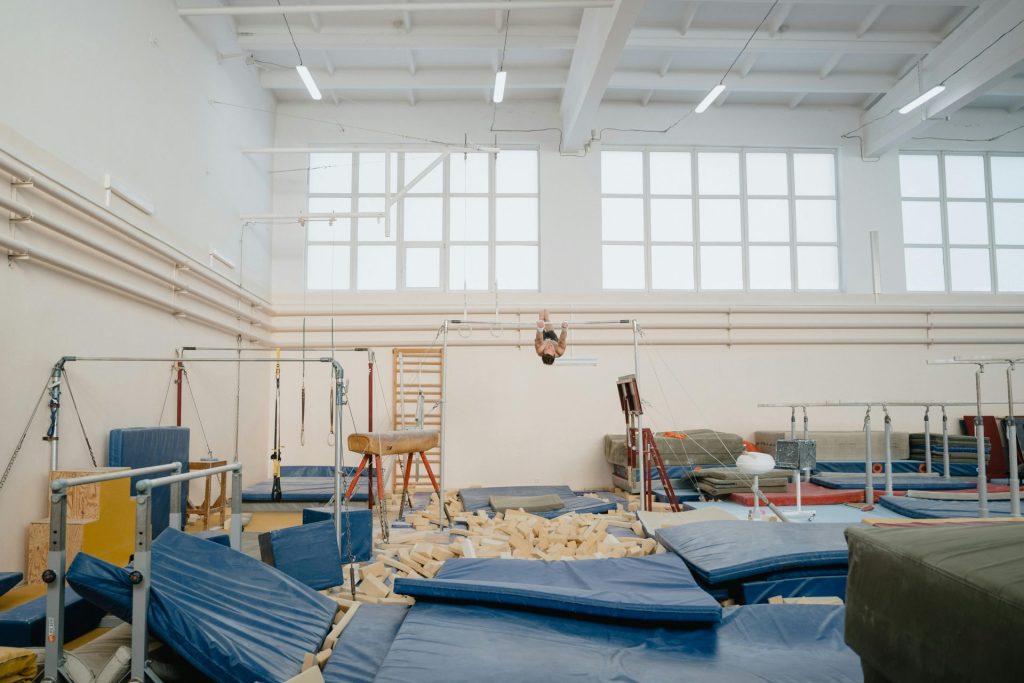 Helle, überdachte Turnhalle mit verschiedenen Geräten und einem trainierenden Athleten.